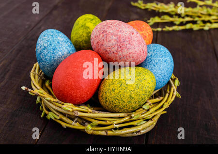 Colorful painted eggs in a nest of twigs of willow on a dark wooden background. Traditionally for Easter. Stock Photo