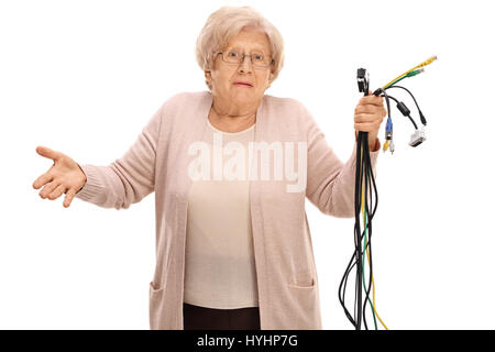 Confused elderly woman holding different types of electronic cables and looking at the camera isolated on white background Stock Photo