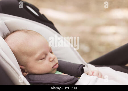 Baby boy fastened with security belt is sleeping peacefully in the car safety seat on the blur brown background, image with toning Stock Photo