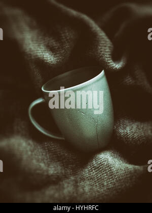 Broken coffee cup pieces has been glued together, green pullover on background Stock Photo