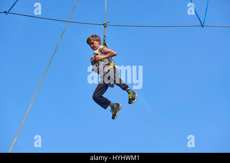 Cute school boy enjoying a sunny day in a climbing adventure activity park. Clear blue sky background. Children summer activities. Stock Photo