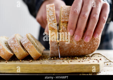 closeup of a young caucasian man cutting a loaf of bread in slices with a knife Stock Photo