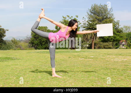 Beautiful woman doing yoga outdoors holding a blank piece of paper. Stock Photo