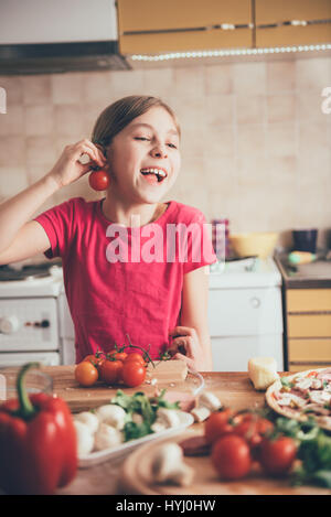 Cute little girl fooling around with tomato in the kitchen Stock Photo