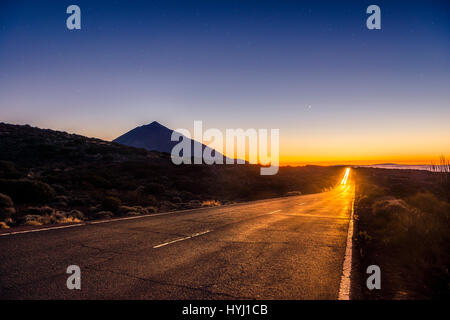 Light trails from car on mountain road, highway, sunset, Vulcano Teide backlit, silhouette, volcanic landscape, starry sky Stock Photo