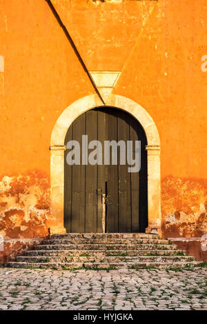 Detail of wooden door in bright orange textured wall and stone stairs Stock Photo