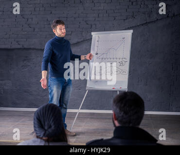 Young speaker man talking to audience during conference. He is giving a lecture and showing graph on flipchart.  Business presentation concept. He is  Stock Photo