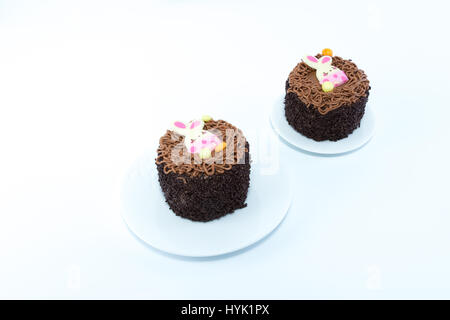 Two small chocolate cakes with Easter bunny detail on white dishes isolated in white background Stock Photo