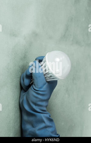 blue rubber glove holding lamp bulb against wall Stock Photo