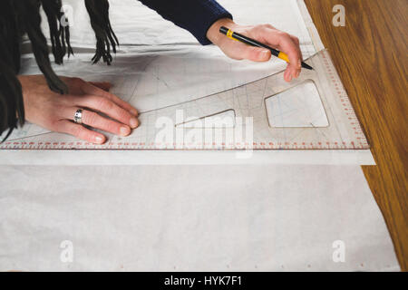 Hands of seamstress drawing templates in tracing paper using rules Stock Photo