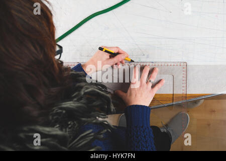Hands of seamstress drawing templates in tracing paper using rules Stock Photo
