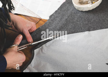 Hands of seamstress cutting a grey fabric with scissors using a paper template Stock Photo