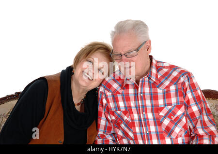 An older senior citizen couple sitting on a sofa, the wife with her head on the shoulder of her husband, isolated for white background. Stock Photo