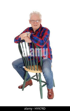A handsome happy senior citizen sitting backwards on a green chair, relaxing, isolated for white background. Stock Photo