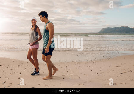 Outdoor shot of young couple on walking along the shore. Young man and woman strolling on beach in morning. Stock Photo