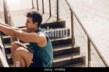 Fitness male doing stretching workout outdoors at the beach. Healthy young man stretching on a railing . Stock Photo