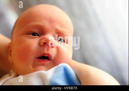 Cute baby girl makes a funny upset face on mothers hand Stock Photo