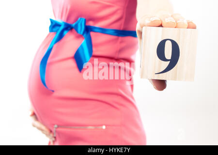 Vintage photo, Pregnant woman in pink dress with blue ribbon showing number of ninth month of pregnancy, concept of extending family and expecting for Stock Photo