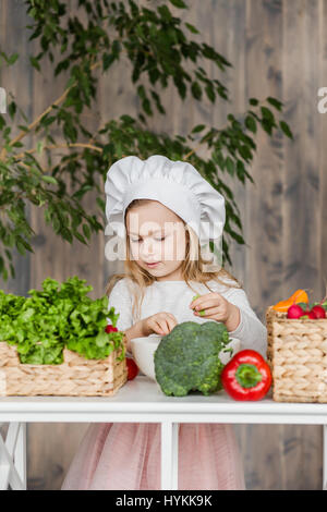 Little beautiful girl making vegetable salad in the kitchen. Healthy food. Little housewife Stock Photo