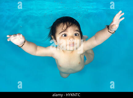 A picture of Aarav, 6 months old, at an underwater photo shoot with Little Fishes Swim School in Bushey, Hertfordshire. SWIMMING before they can walk these little bathing beauties have been photographed underwater by a British photographer. Utilising their natural amphibious reflex, these babies, aged from just three months old, held their breath as they were released underwater by professional baby swim instructors.  Photographs show the hilarious expressions on the faces of the little nippers. London based underwater photographer Lucy Ray (35) from Starfish Underwater Photography took these  Stock Photo