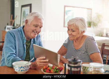 Smiling seniors using a digital tablet together over breakfast Stock Photo