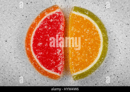 Two colorful marmalade slices in the form of citrus fruits. They lay on the gray table-top. Stock Photo