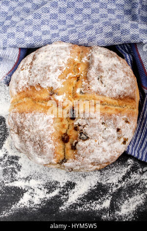 irish fruit soda bread with flour and kitchen towel on slate Stock Photo