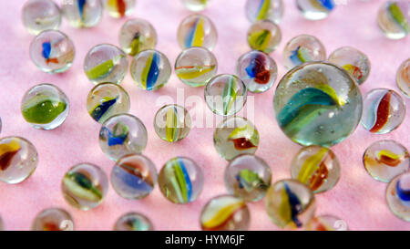 one big marble and several small ones on pink table Stock Photo