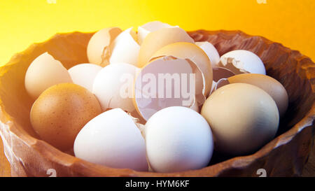 wooden bowl with empty broken egg shells on yellow background Stock Photo
