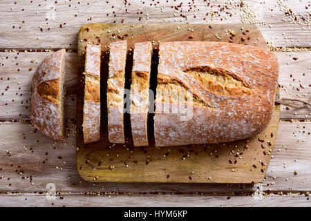 high-angle shot of a loaf of spelt bread cut in some slices on a chopping board, placed on a white rustic wooden table Stock Photo
