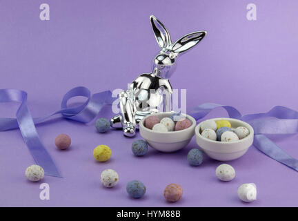 Easter egg background with silver rabbit, lilac satin ribbon and speckled chocolate eggs isolated on violet Stock Photo