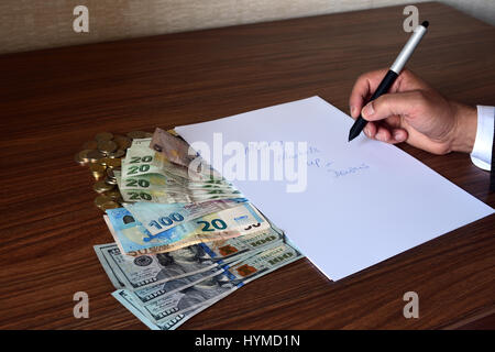 arm of business person in jacket holding a pen with euros, liras and US dollars on table next to note paper Stock Photo