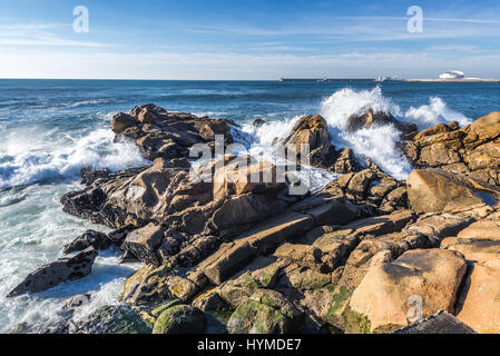 Rocks on the beach in Nevogilde civil parish of Porto, Portugal. Port of Leixoes Cruise Terminal building on background Stock Photo