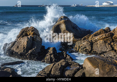 Waves smashing against rocks on the beach in Nevogilde civil parish of Porto, Portugal. Port of Leixoes Cruise Terminal building on background Stock Photo