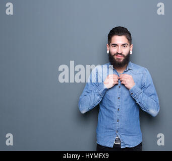 Portrait of a handsome young man adjusting buttons on shirt posing on gray background Stock Photo