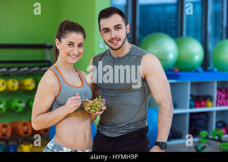 Happy couple in gym feeding each other with fresh salad Stock Photo