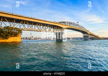 Auckland Harbour Bridge in evening light with yachts passing under. Stock Photo
