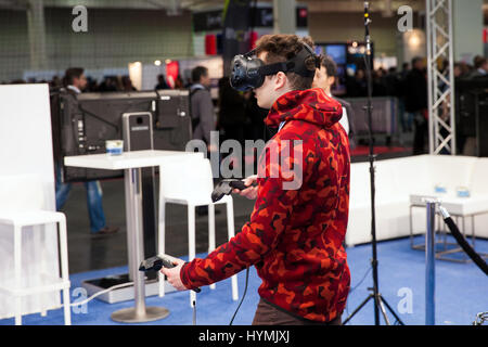 Man playing video game in virtual reality headset and handheld controllers developed by HTC Vive on exhibition Cebit 2017 in Hannover Messe, Germany Stock Photo