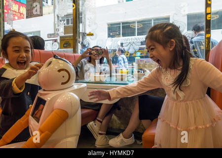 Girls interacting with robot waiter at a restaurant in Hong Kong while mother looks on Stock Photo