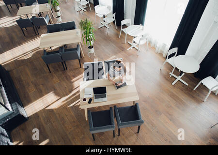 Overhead view of young female working on her laptop at a cafe. Top view shot of female sitting at a table with a cup of coffee browsing internet. Stock Photo
