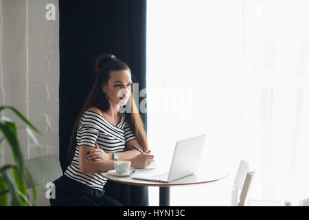 Young woman writer working at the cafe with notebook and laptop, drinking cappuccino. Stock Photo