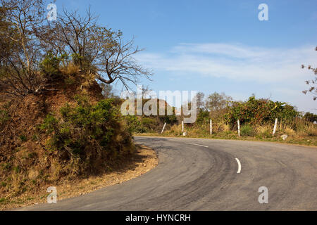 a hairpin bend in the road going through morni hills nature reserve near chandigarh in india with vegetation and trees under a blue sky Stock Photo