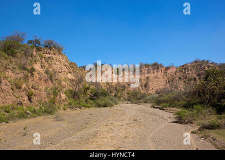 a dry river bed with orange sandy cliffs in the nature reserve of morni hills near chandigarh india under a blue sky Stock Photo