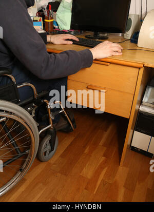 young disabled man in a wheelchair using the computer with mouse on the desk Stock Photo