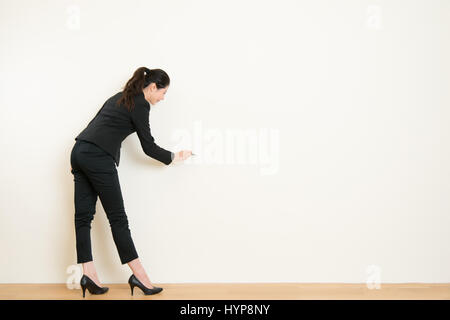 back of young business asian woman in with pen drawing or writing on empty wall. business idea and concept Stock Photo