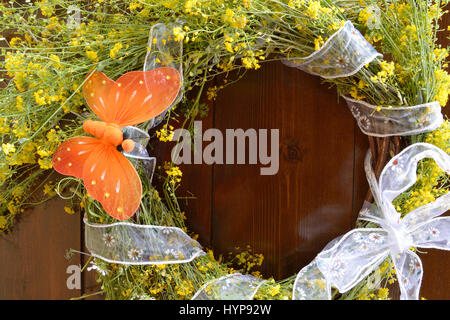 Wreath of yellow wild flowers and decorated with an orange butterfly on wooden background Stock Photo