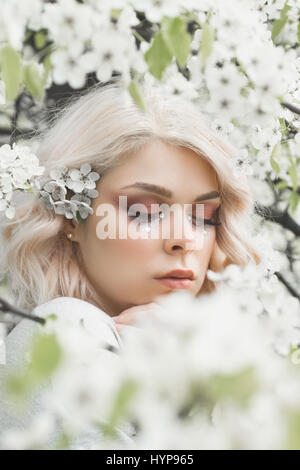 Lovely girl with curly blonde hair in spring floral garden, clear good warm day. Spring time. Stock Photo