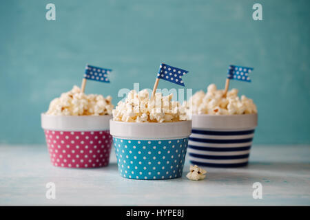 Homemade buttered popcorn served in colorful bowls decorated with party flags. Popcorn arranged in striped and spotted bowls. Stock Photo