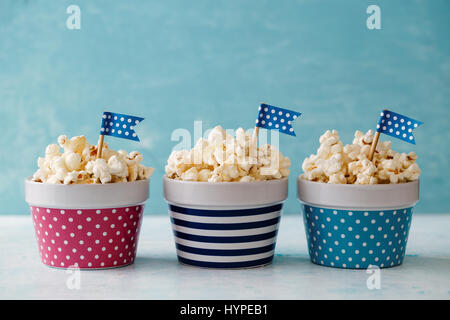 Homemade buttered popcorn served in colorful bowls decorated with party flags. Popcorn arranged in striped and spotted bowls. Stock Photo