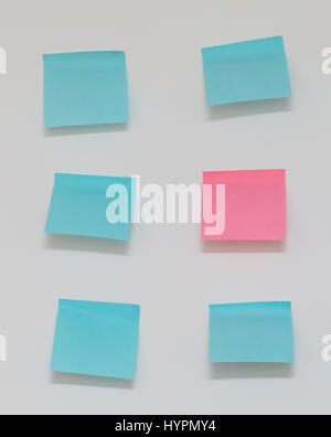 Single pink post it note in sea of blue post it notes Stock Photo